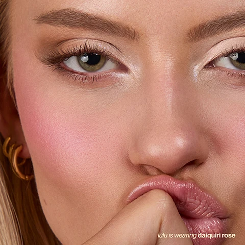 Image 1 - A close-up of a womans face with green eyes, rosy pink blush on her cheeks, and a finger touching glossy pink lips, with the text lulu is wearing daiquiri rose. Image 2 - A swatch of pink, textured cream features overlaid text: Avocado Oil ultra-nourishing and creamy, African Yellow Wood Bark Extract helps fix excess oil production, Blurring Microspheres a must-have for that dream-skin finish. Image 3 - A smiling person with dark hair and eyes closed wears blush and lip gloss, with text that reads how to use Swipe onto cheeks, then blend upward with fingers, a brush, or sponge. Build for more intensity, or dab on lips and lids for a soft-focus finish. Image 4 - Three cylindrical makeup sticks in peachy-orange, vibrant rose, and soft petal-pink are stacked on a white background, with text on the left that reads: Pick your favorite cocktail-inspired shade or mix your own custom blend. mimosa bloom peachy tones cosmo blossom vibrant rose daiquiri rose soft petal-pink. Image 5 - Three cosmetic stick products in shades of pink, mauve, and coral with gold casings are shown with text that reads customisable colour, Three wearable shades that mix and match for your perfect, personalised flush, seamless blending, Cream-to-powder formula layers flawlessly with any base, and multi-use & portable, helps fix excess oil production. Image 6 - A textured pink background resembling cream blush or makeup with streaks, featuring four customer reviews: JUST GORGEOUS! (5 stars) This is literally the best cream blusher Ive ever tried! It looks amazing every time - Kelly. LONG LASTING! (5 stars) This beauty of a blush glides on, smudges in well and can be built up if a darker blush is needed. It lasts all day long and is my new favourite blush - Jayne. AMAZING BLUSH (5 stars) This is an amazing product.... it glides onto your skin and blends in perfectly... it is so smooth and the colour is gorgeous - Ellie. EXTRAORDINARY (5 stars) This is gorgeous! The consistency is beautiful, goes on so smoothly and blends perfectly - superb colour and now I want another one in another colour! - Sarah. Image 7 - A four-panel image features an Iconic London blurring blush stick in a waffle cone with pink ice cream, and three close-up portraits of models demonstrating blush shades: a person wearing Daiquiri Rose, another wearing Mimosa Bloom, and a third wearing Cosmo Blossom, with accompanying text Blurring Blush Stick, Daiquiri Rose, Mimosa Bloom, Cosmo Blossom. Image 8 - A close-up portrait of a woman with blonde hair and hazel eyes, showcasing a vibrant pink blush on her cheeks and glossy lips, with her hand gently touching her face, and the text lulu is wearing mimosa bloom in the bottom right. Image 9 - A blonde woman with rosy blush on her cheeks and puckered pink lips looks to the right while her finger with a French manicured nail touches her cheek, and text says lulu is wearing cosmo blossom.