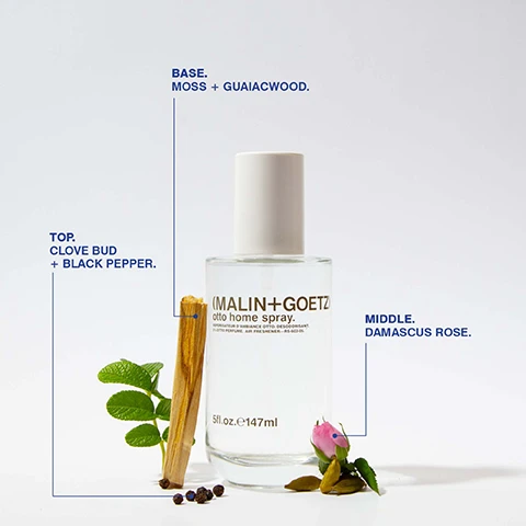 Image 1 - A glass bottle of MALIN+GOETZ Otto home spray is displayed with a white cap, surrounded by a piece of guaiacwood, green leaves, black peppercorns, and a small pink rosebud, with labels indicating the top notes of clove bud and black pepper, middle note of Damascus rose, and base notes of moss and guaiacwood.
Image 2 - A hand holds a spray bottle labeled CLEAN + GOETZ while spraying a surface, with the text at the top stating it eliminates 95% of unwanted smells + creates lasting freshness for up to 2 hours and a note at the bottom about an independent study.